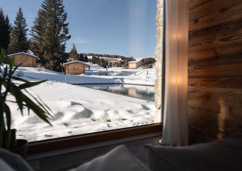 Blick aus dem Ruheraum auf den beheizten Außenpool und die verschneite Landschaft der Seiser Alm