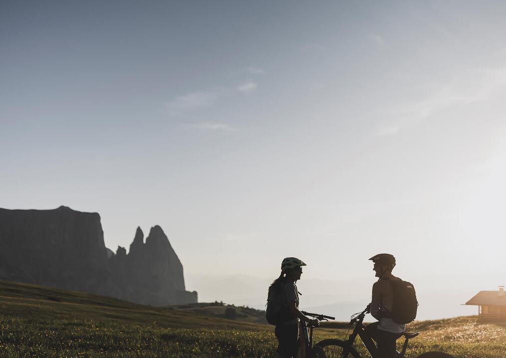 Couple on e-bikes at sunset on Alpe di Siusi Seiser Alm with Mount Schlern in the background