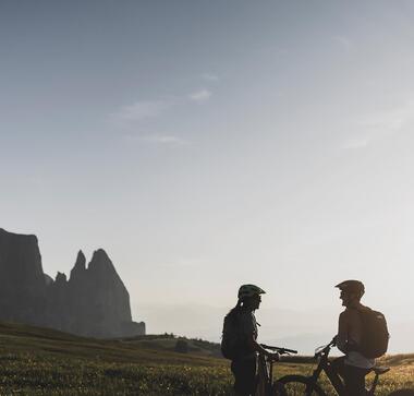 Couple on e-bikes at sunset on Alpe di Siusi Seiser Alm with Mount Schlern in the background