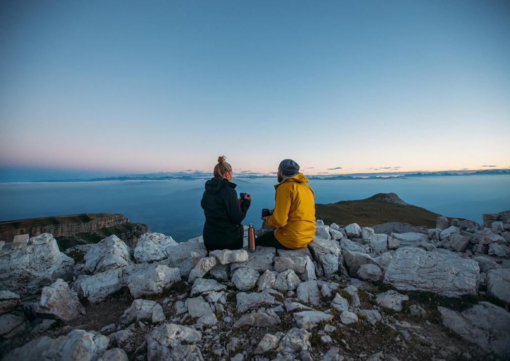 Couple enjoying sunrise coffee on a mountain peak above the clouds in the Dolomites near Alpe di Siusi Seiser Alm