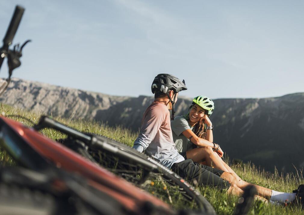 Couple taking a break during a mountain bike tour on the meadows of Alpe di Siusi Seiser Alm