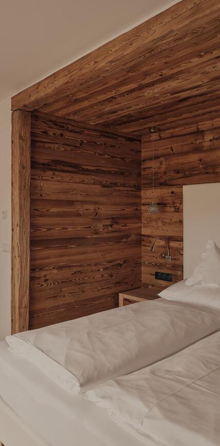 Doppelbett mit Altholzwänden und angrenzendem Badezimmer im Sporthotel Floralpina