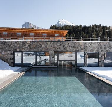 Hotel Floralpina mit Außenpool, verschneiten Wiesen und Blick auf die Dolomiten