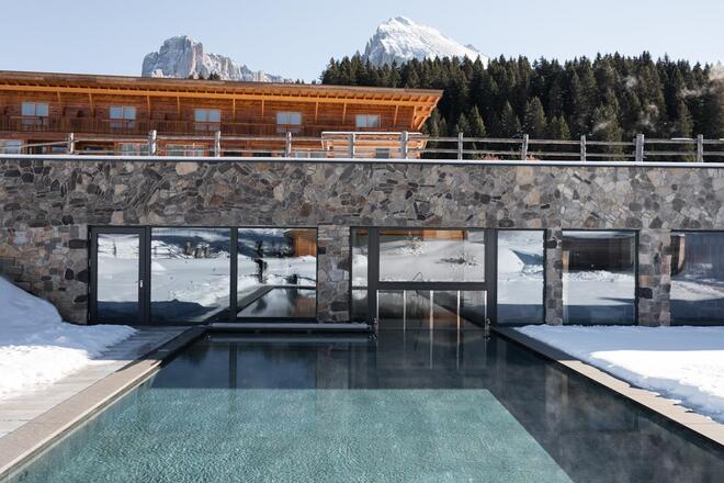 Hotel Floralpina mit Außenpool, verschneiten Wiesen und Blick auf die Dolomiten