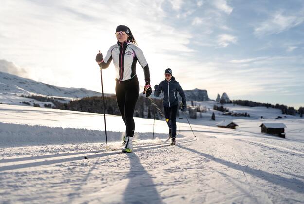 Cross-country skiers on a groomed trail on Alpe di Siusi Seiser Alm with Mount Schlern in the background