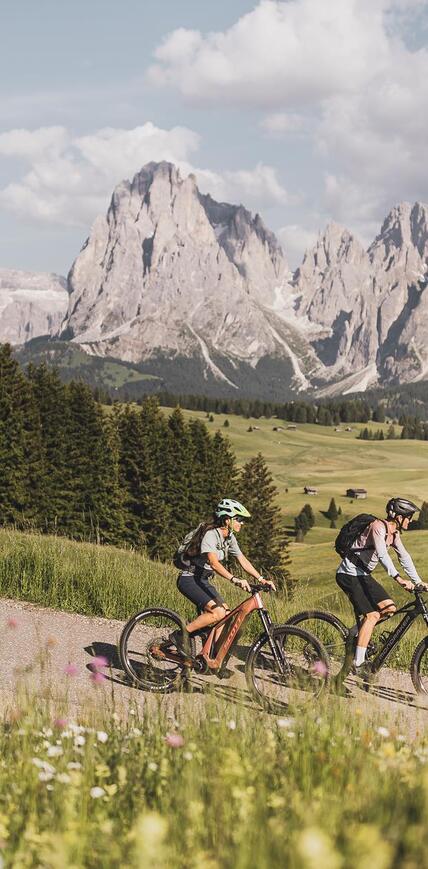 ouple on an e-bike tour across Alpe di Siusi Seiser Alm with views of Langkofel and Plattkofel in the Dolomites