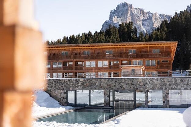 Heated outdoor pool at Hotel Floralpina surrounded by snow, forest and Dolomites scenery