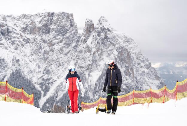 Couple with sleds tobogganing on Alpe di Siusi Seiser Alm with the snowy Mount Schlern in the background