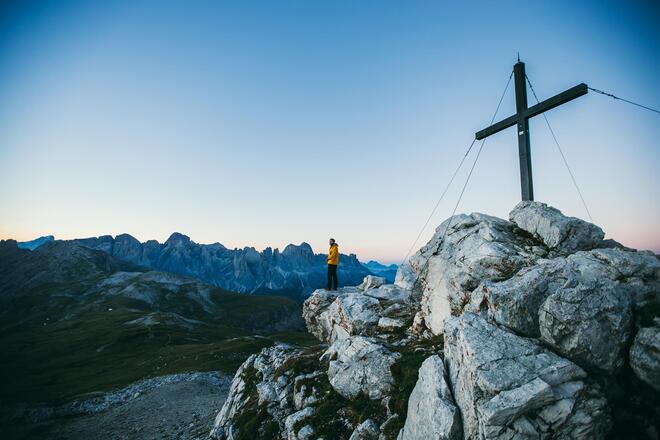 Wanderer am Gipfelkreuz auf einem Bergmassiv der Dolomiten nahe der Seiser Alm