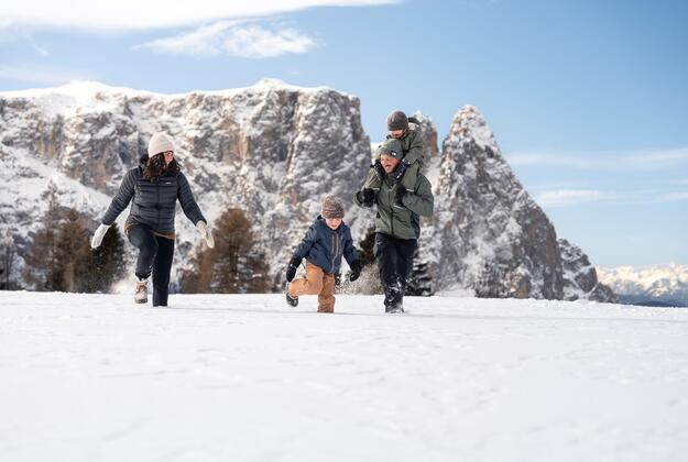 Family with children playing in the snow on Alpe di Siusi Seiser Alm with the snowy Dolomites in the background