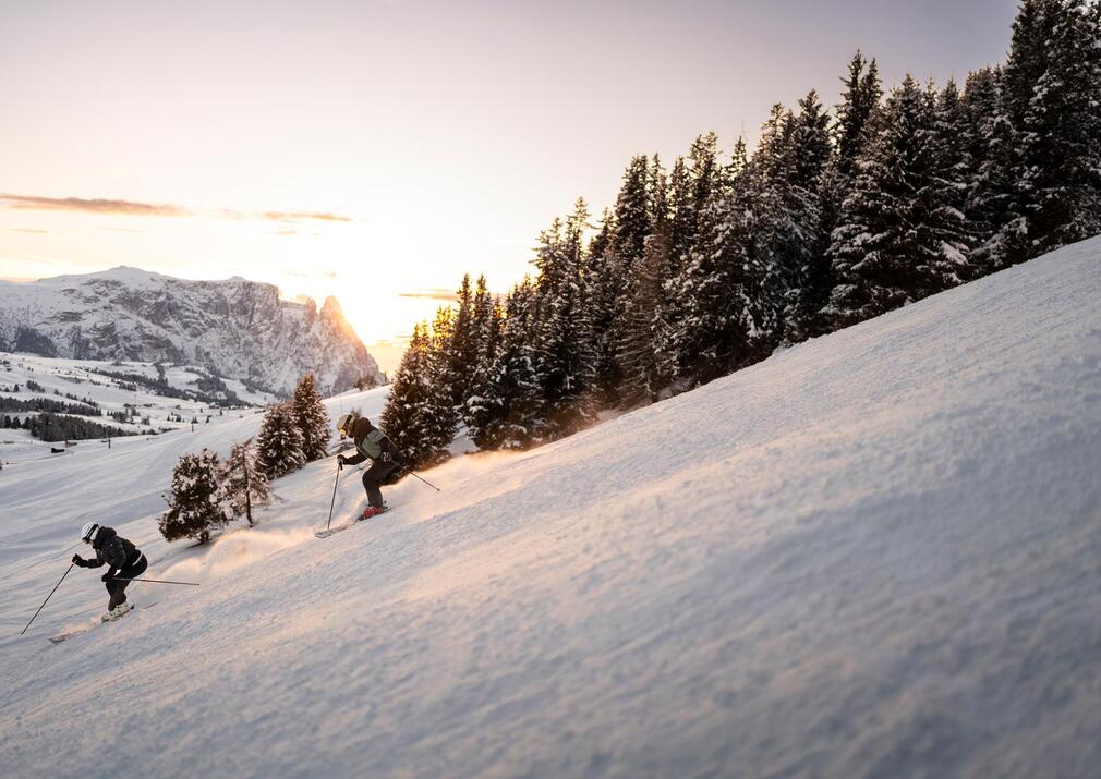 Skiers at sunset carving down a slope on Alpe di Siusi Seiser Alm with Mount Schlern in the background