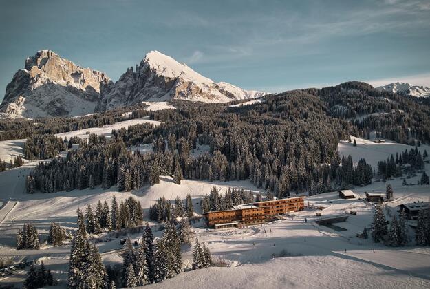 Vista aerea invernale dello Sporthotel Floralpina sull'Alpe di Siusi con Sasso Lungo e Sasso Piatto